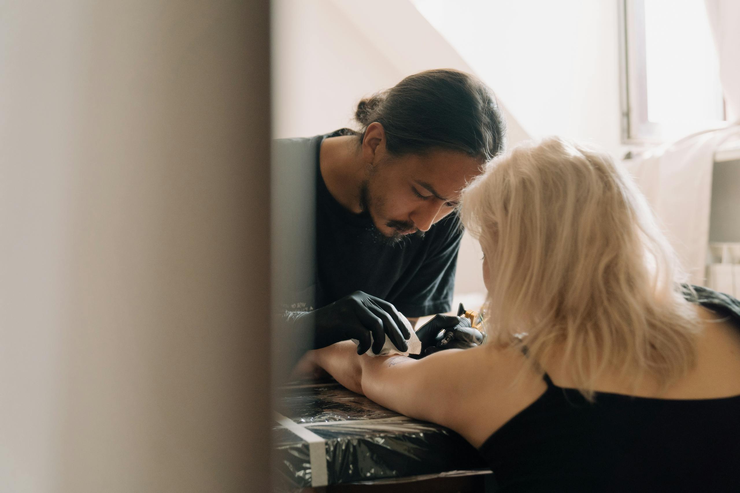A tattoo artist carefully creating a design on a client's arm inside a studio.