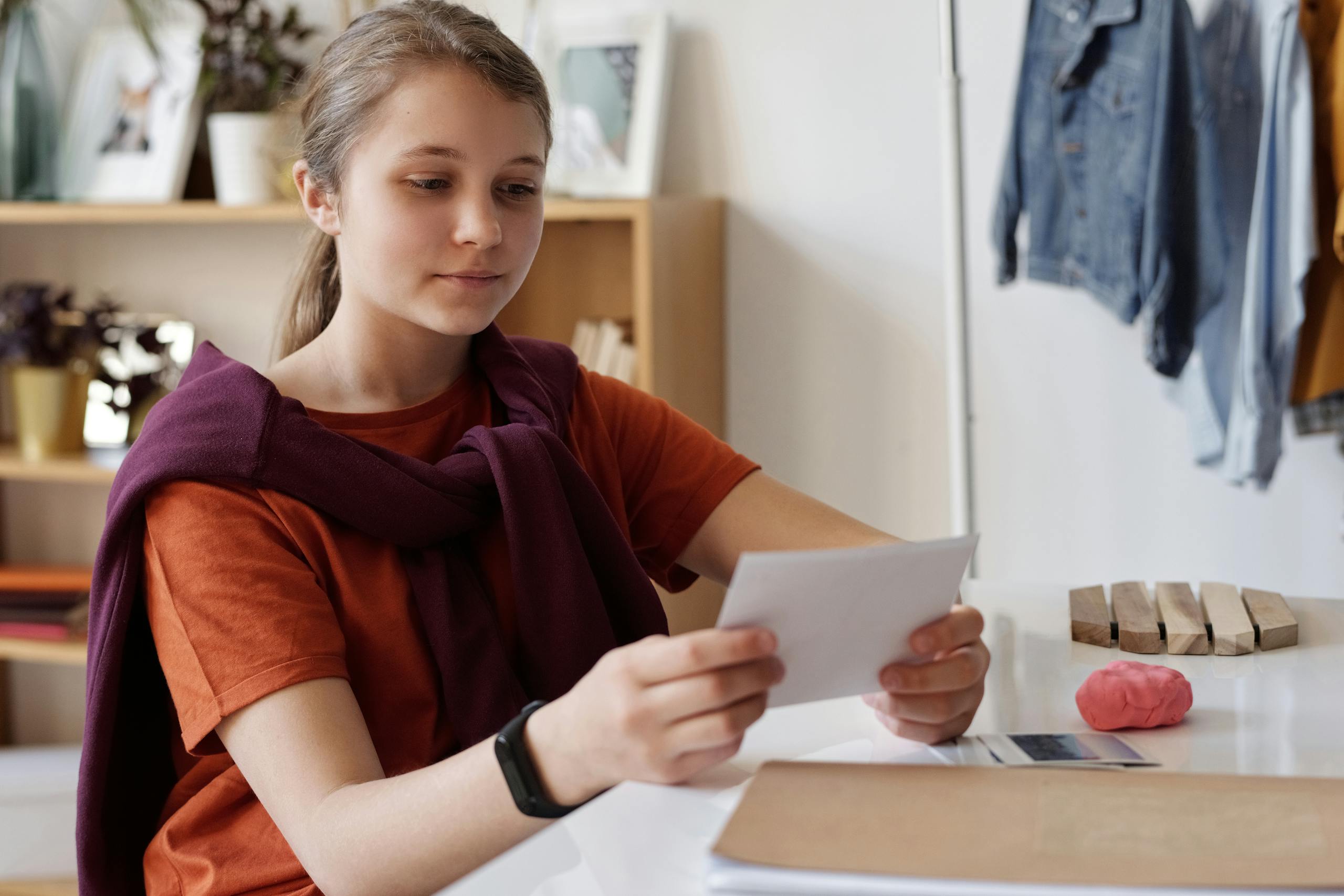 A teenage girl thoughtfully examines photos at her desk, lost in memories.