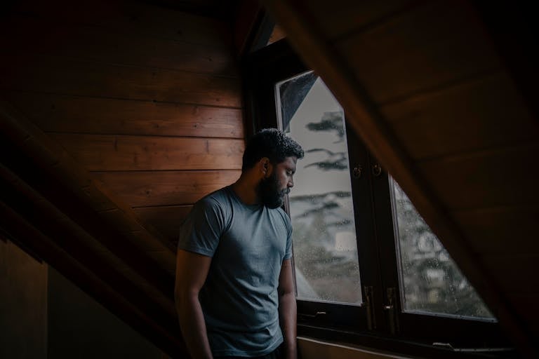 A thoughtful man stands by a window, lost in contemplation, indoors in Sri Lanka.