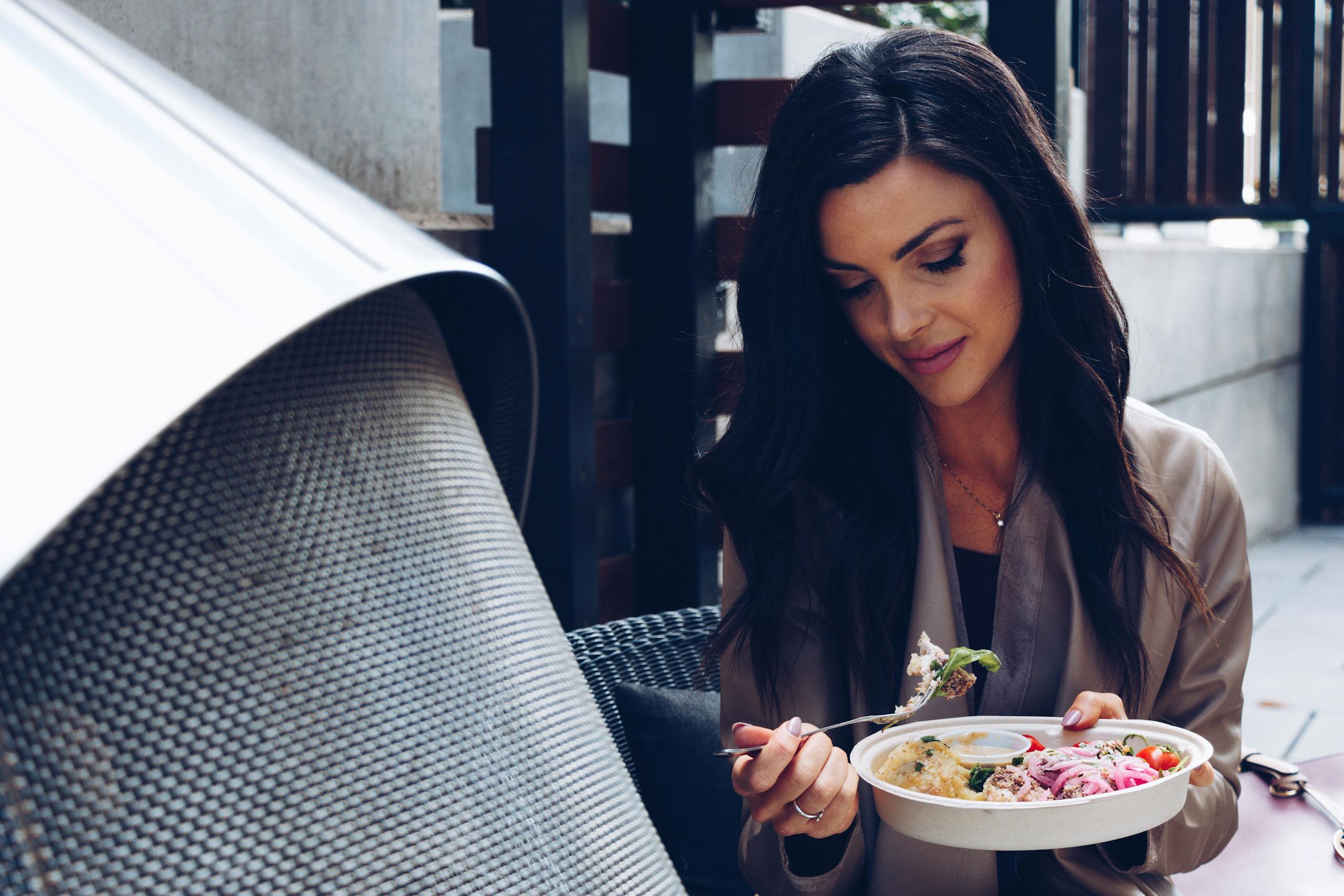 A woman enjoys a nutritious salad in an outdoor setting, capturing a moment of healthy lifestyle.