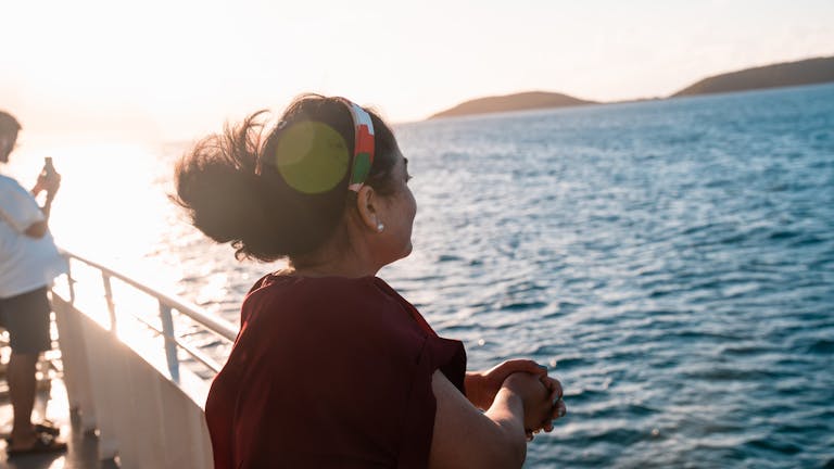 A woman gazes out over the ocean as the sun sets, creating a warm, peaceful ambiance.