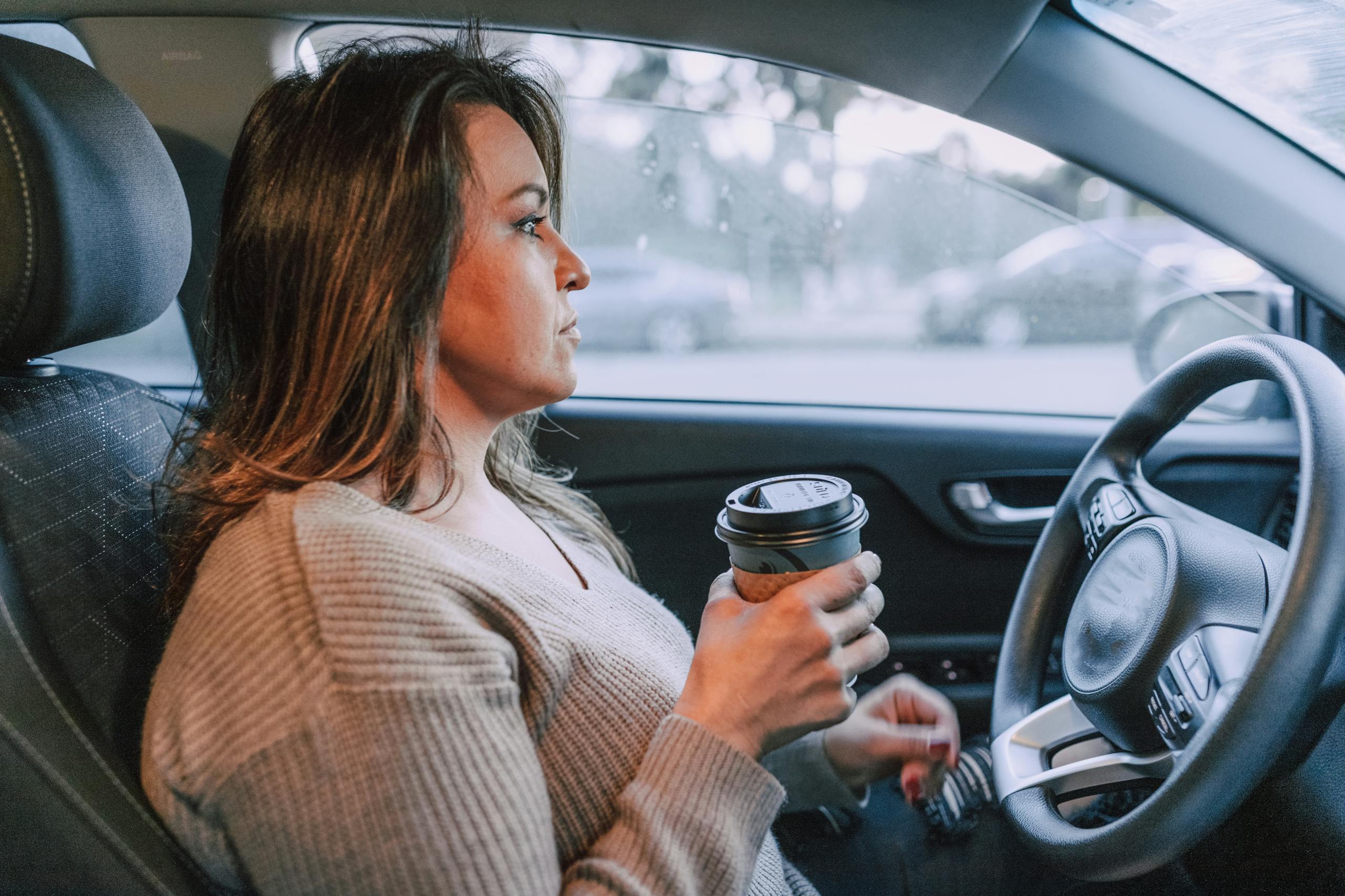 A woman in a car holding a disposable coffee cup, showing focus.