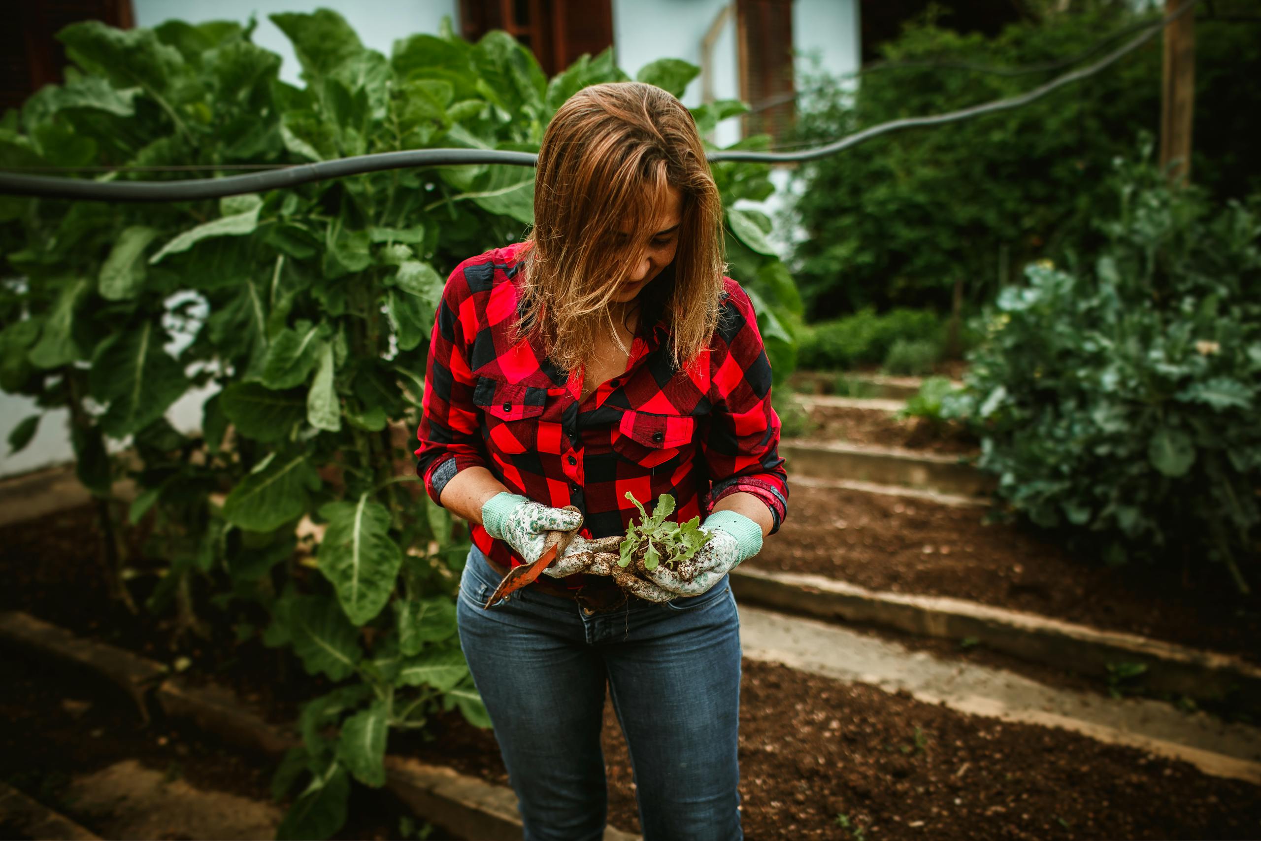 A woman in a plaid shirt tends to her garden, showcasing lush greenery.