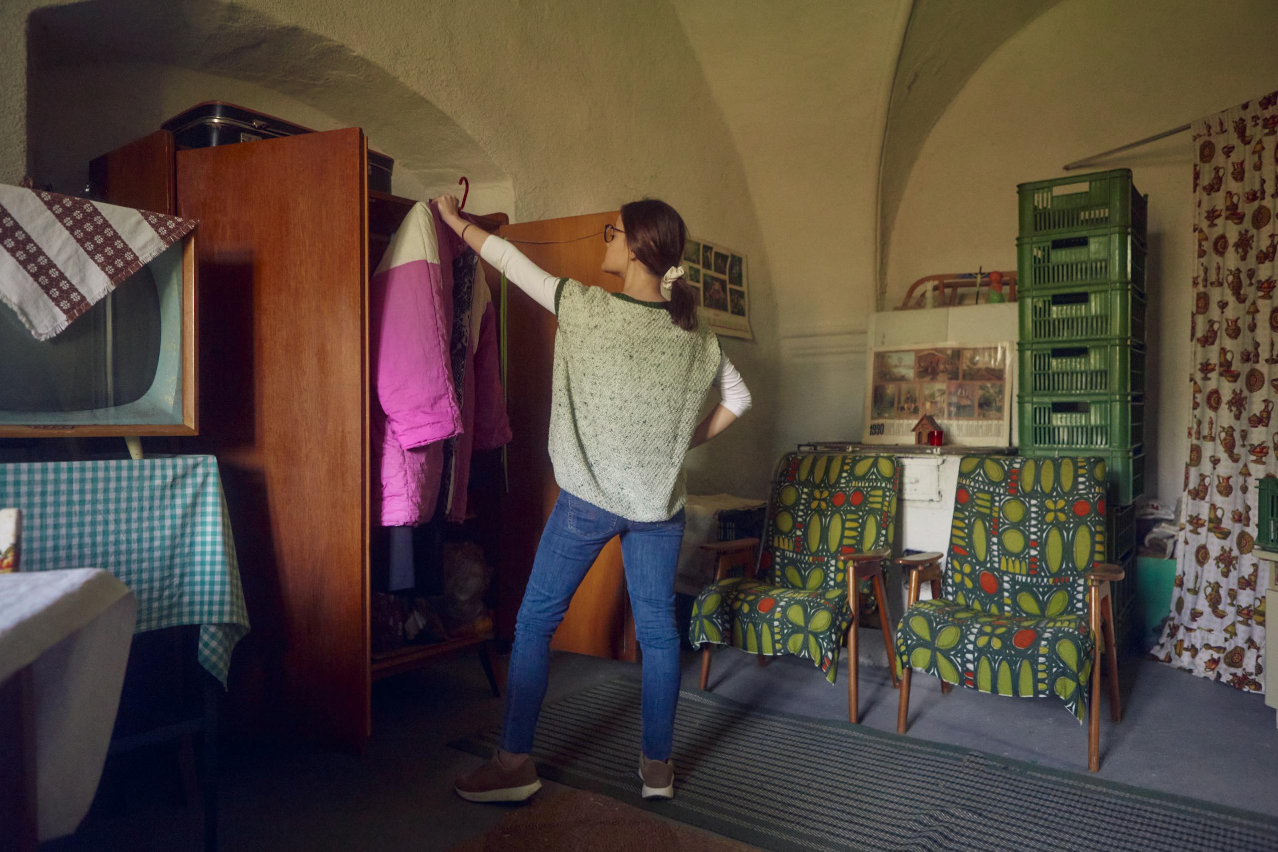 A woman organizing her wardrobe in a vintage-style room with retro furniture and decor.