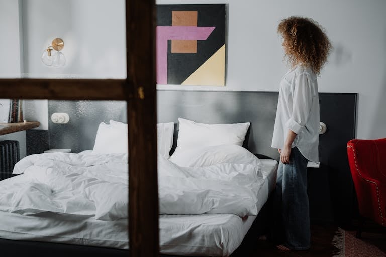 A woman standing in a cozy bedroom with modern art, showcasing a comfortable and stylish interior.