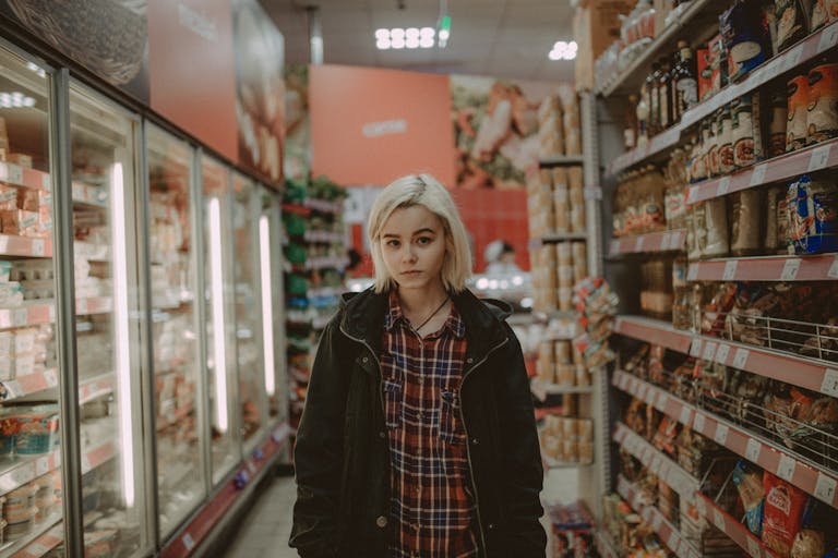 A woman with white hair stands between shelves in a supermarket aisle, showcasing a variety of products.