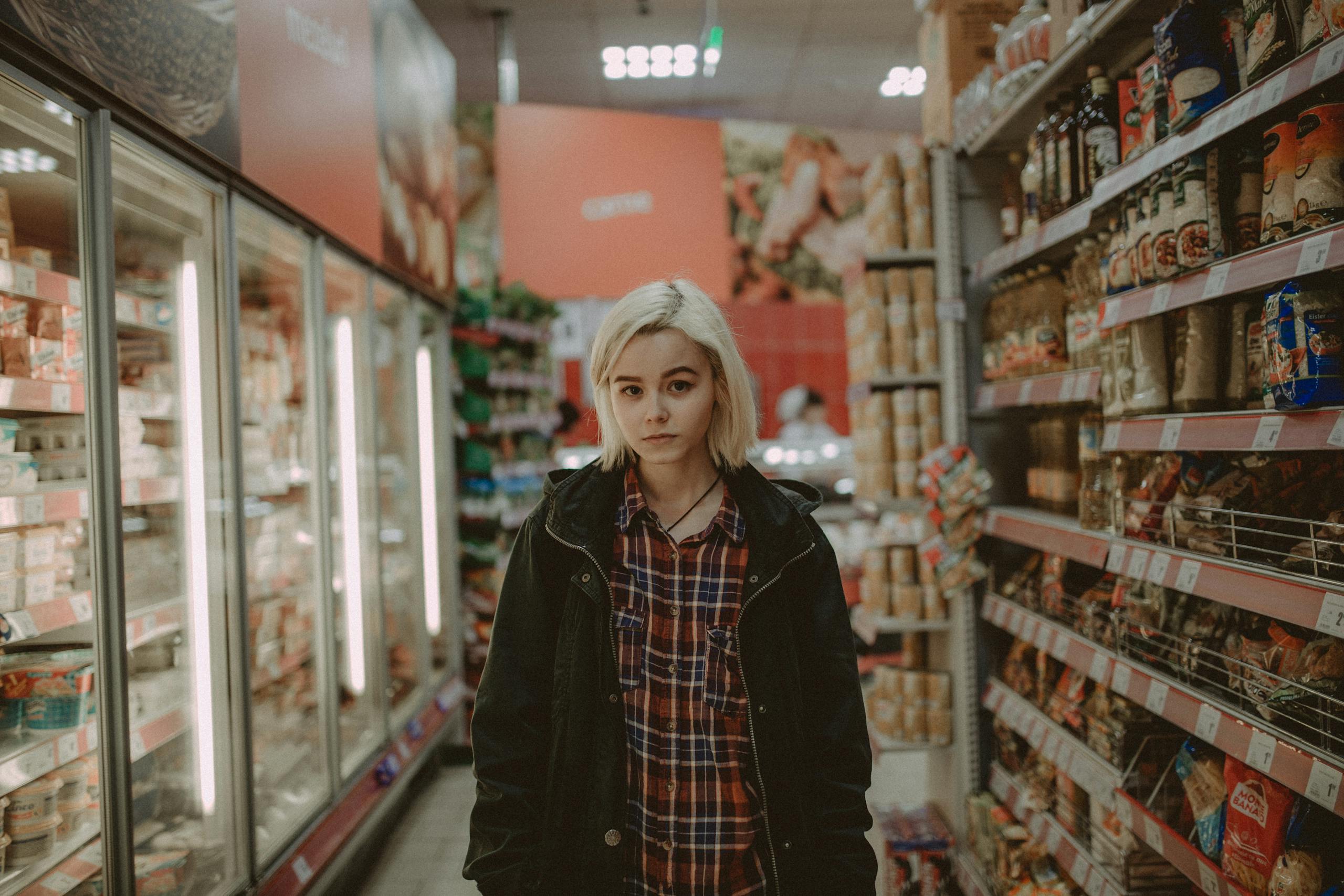 A woman with white hair stands between shelves in a supermarket aisle, showcasing a variety of products.