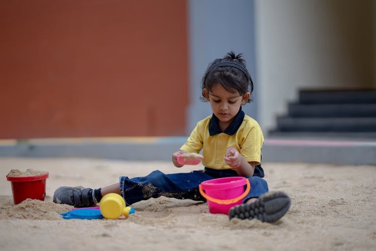 A young child plays in the sandbox, exploring creativity with sand toys outdoors.