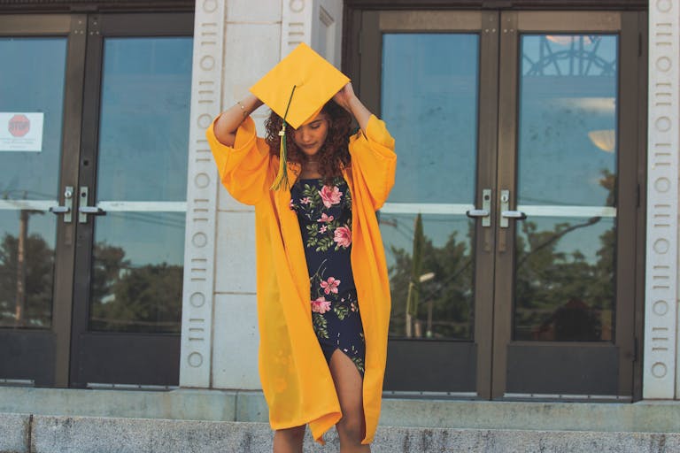 A young woman in a yellow graduation gown celebrating her academic achievement outdoors.