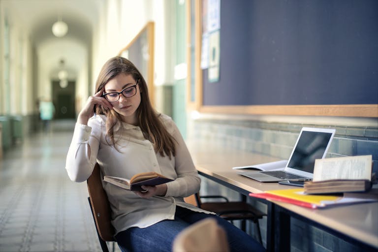 A young woman studies diligently in a university hallway, reading a book.