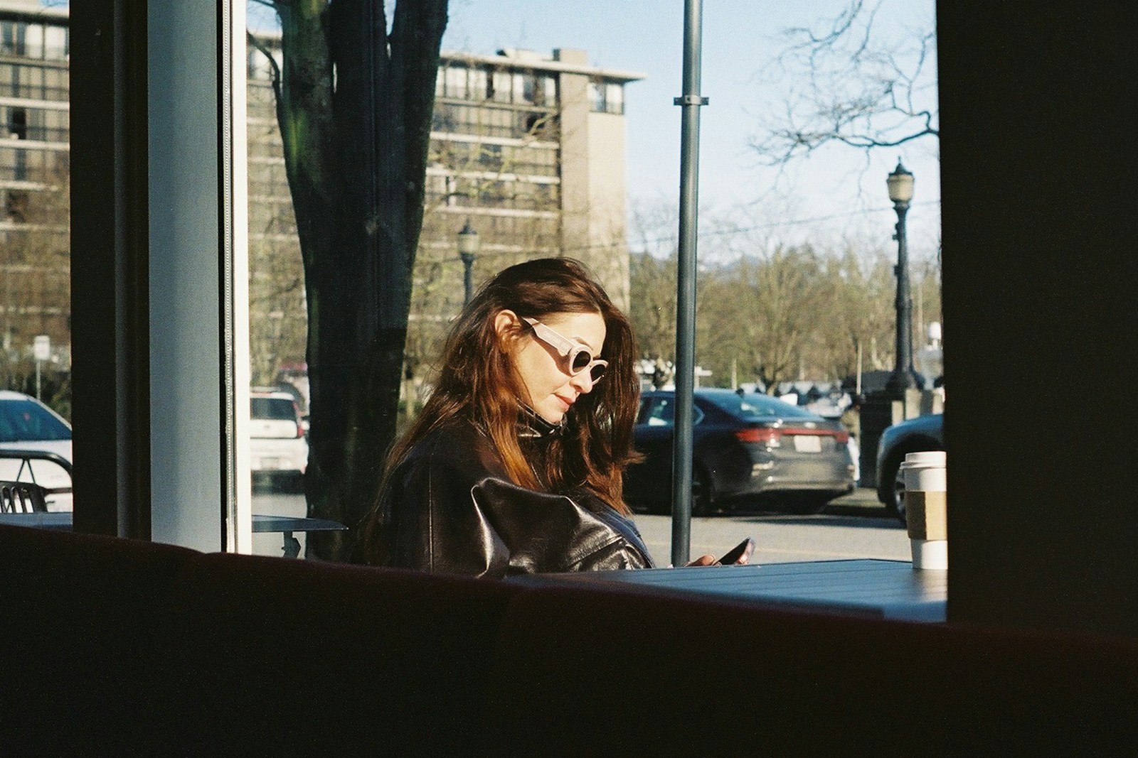 Woman looking at phone inside cafe with cars outside
