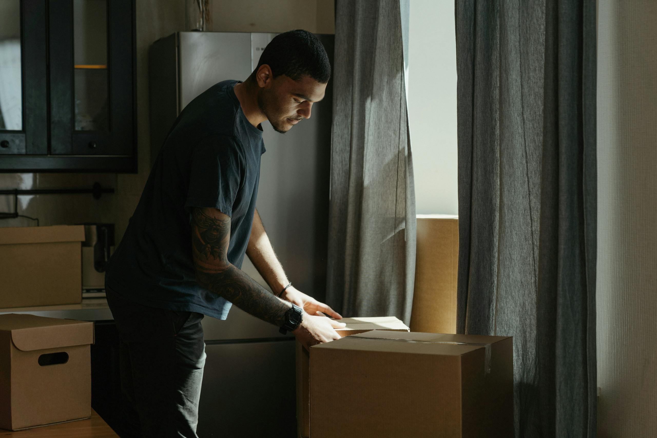 Adult man packing and unpacking boxes in a modern apartment setting.