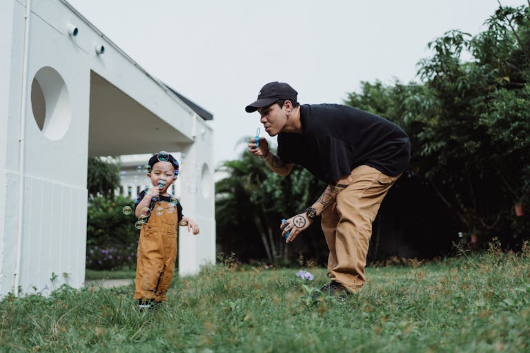 Asian father and son enjoying a playful moment blowing bubbles in the backyard.