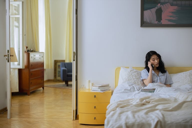 Asian woman in a comfortable home bedroom setting having a phone call.