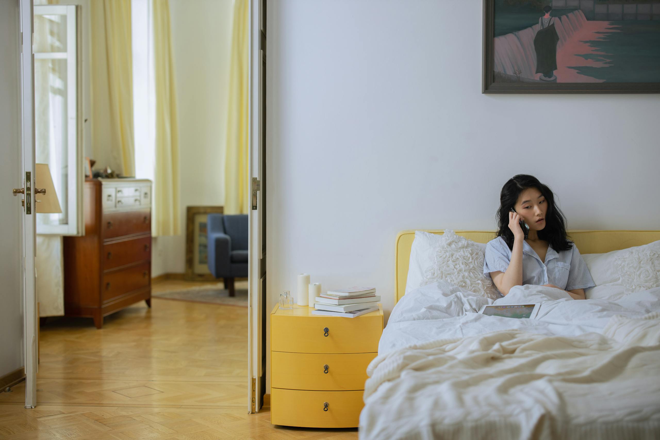 Asian woman in a comfortable home bedroom setting having a phone call.