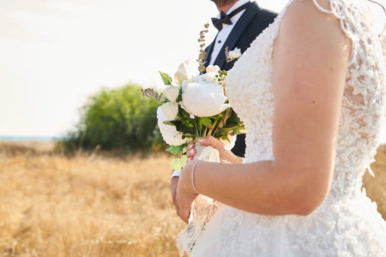 Bride and groom in elegant attire holding a bouquet in a scenic outdoor setting.