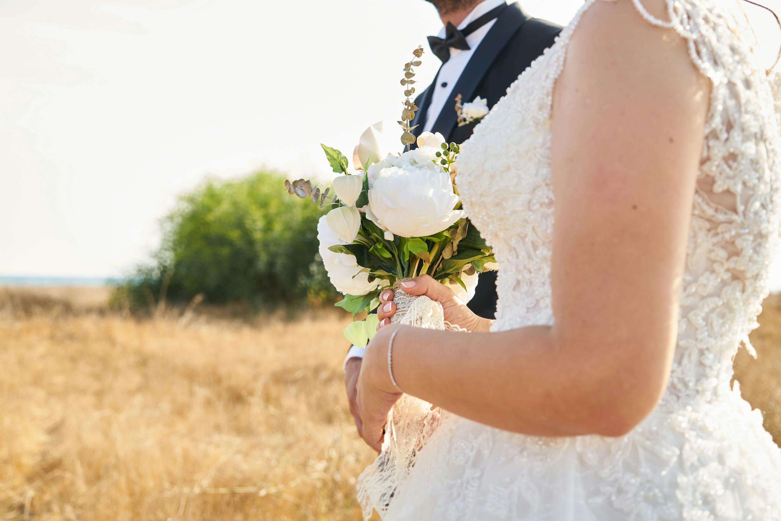Bride and groom in elegant attire holding a bouquet in a scenic outdoor setting.