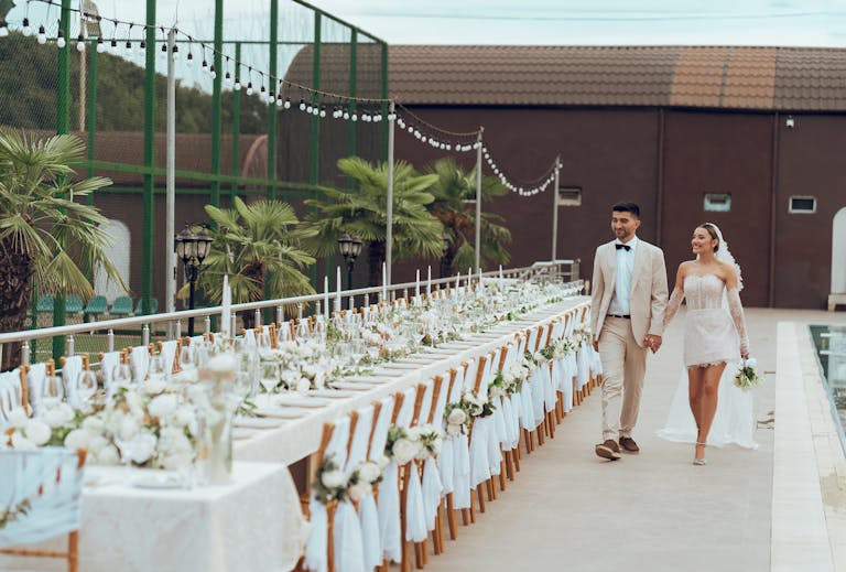 Bride and groom walking past an elegantly set table at an outdoor wedding reception.