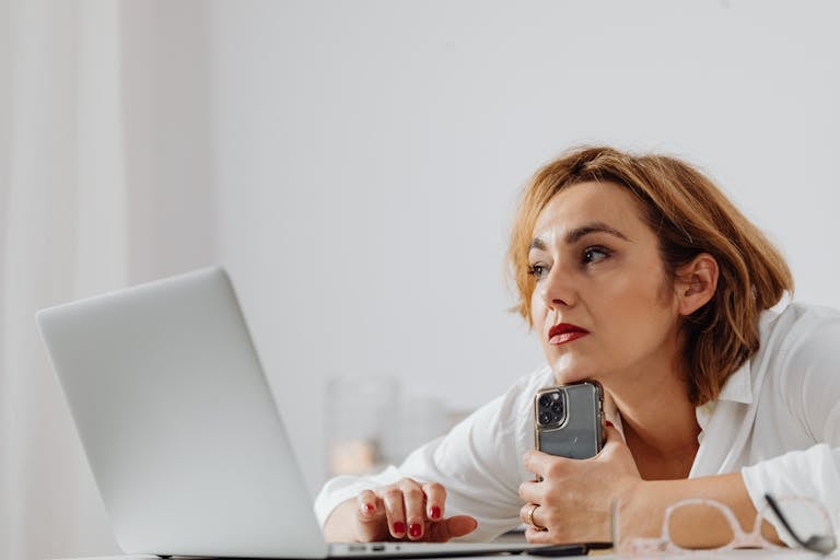 Businesswoman using laptop and mobile phone at modern office desk.