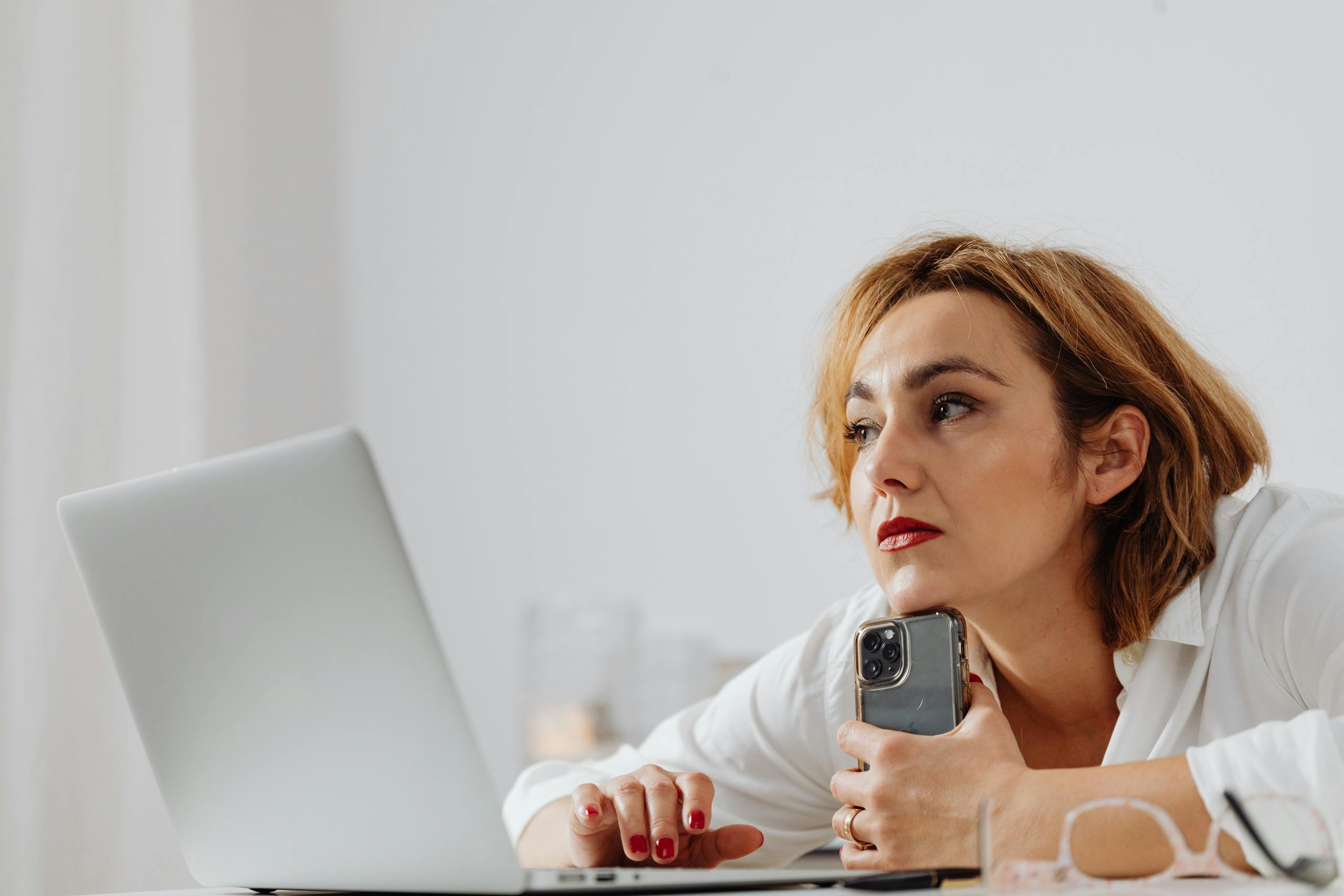 Businesswoman using laptop and mobile phone at modern office desk.