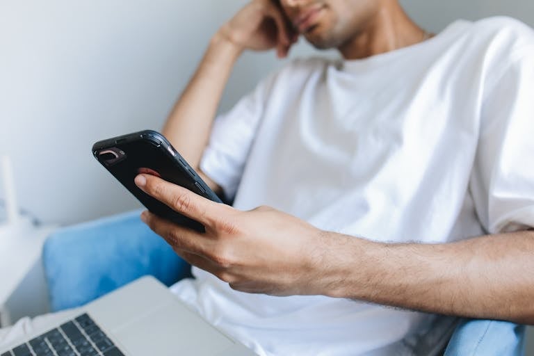 Casual young man in a white t-shirt using a smartphone while seated indoors.