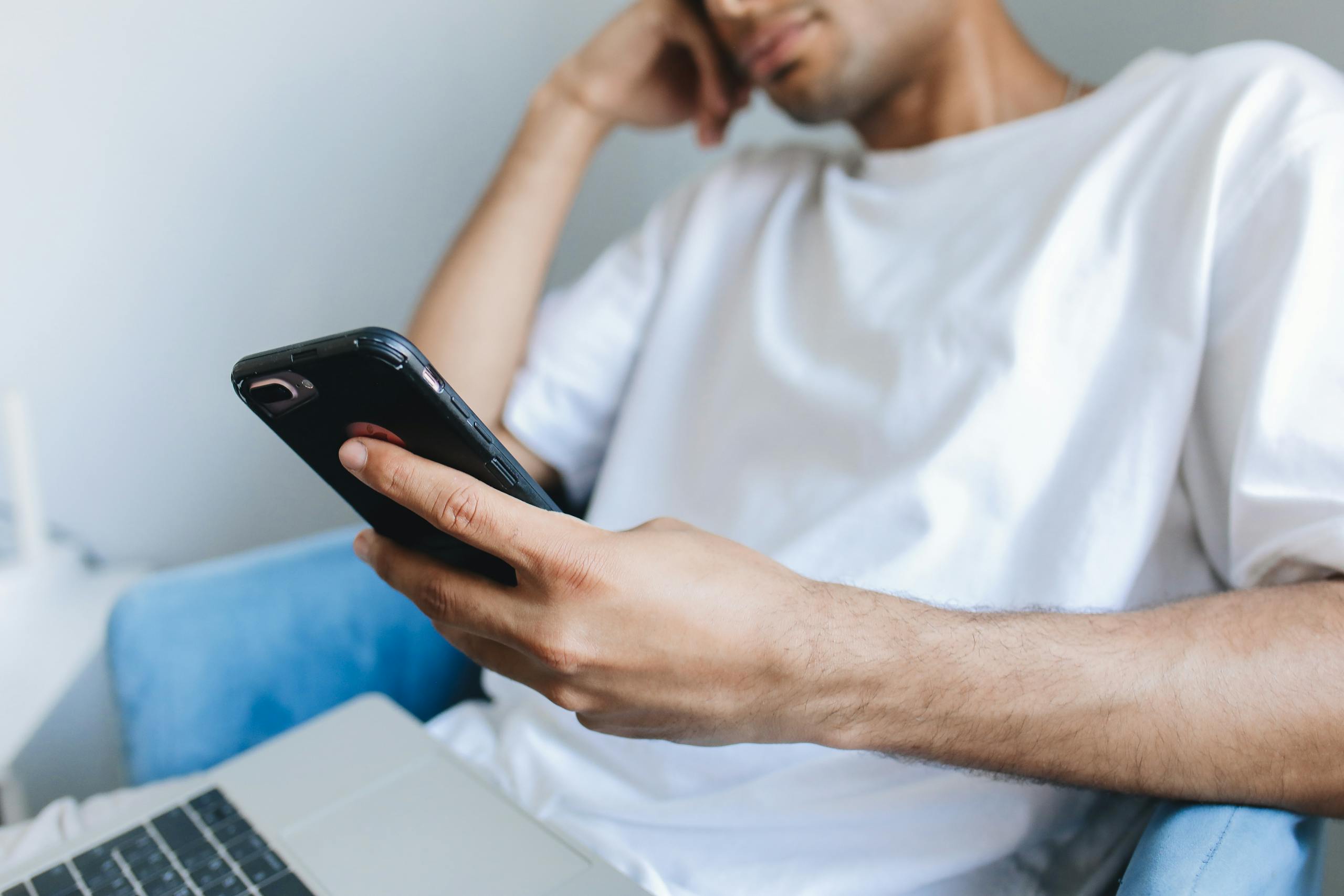 Casual young man in a white t-shirt using a smartphone while seated indoors.