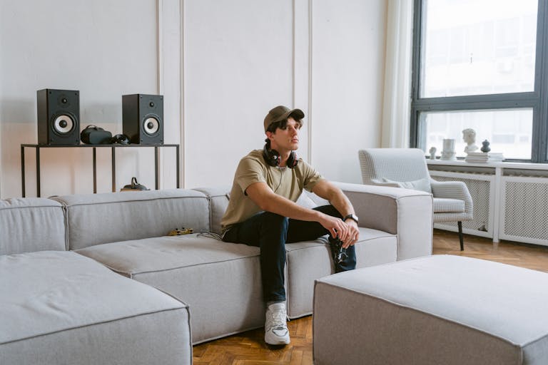 Casual young man wearing headphones sitting on a sofa in a stylish living room with speakers.
