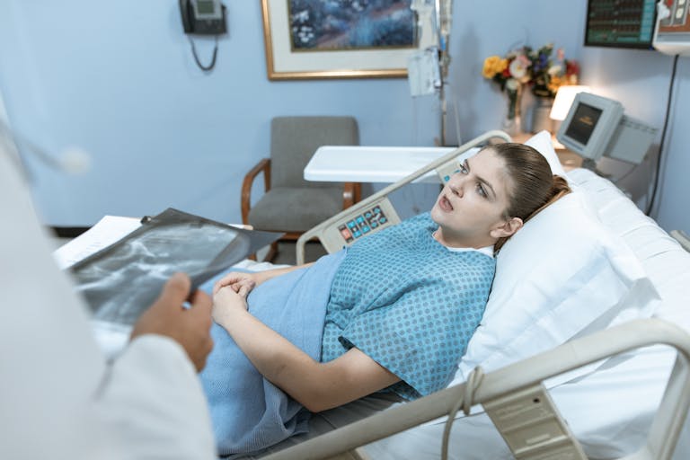 Caucasian woman in hospital bed receiving care from healthcare professional.