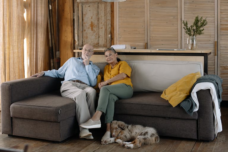 Charming scene of an elderly couple enjoying a cozy moment with their dog on a sofa in a rustic home.