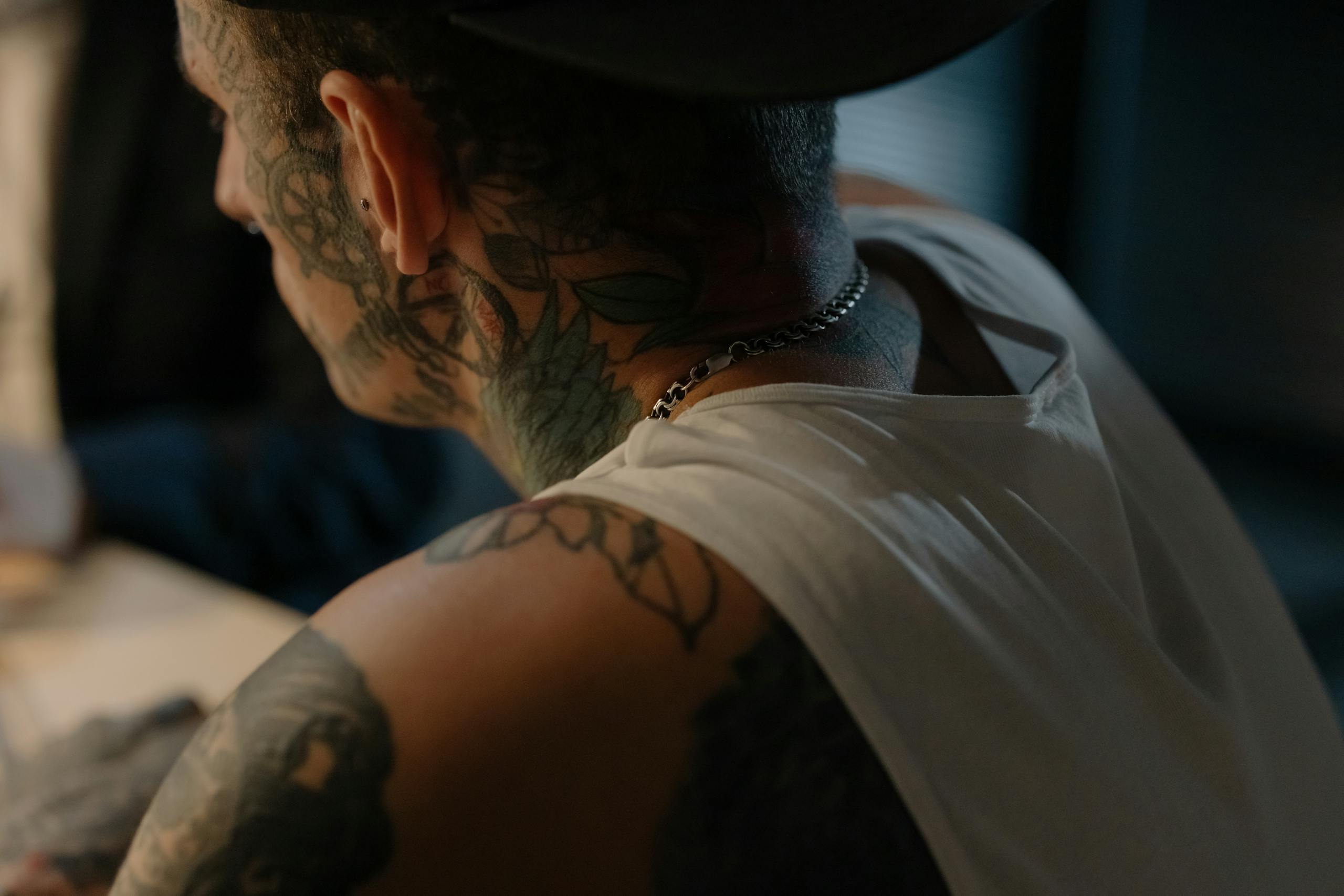 Close-up of a tattooed man in a tank top indoors, showcasing intricate body art.