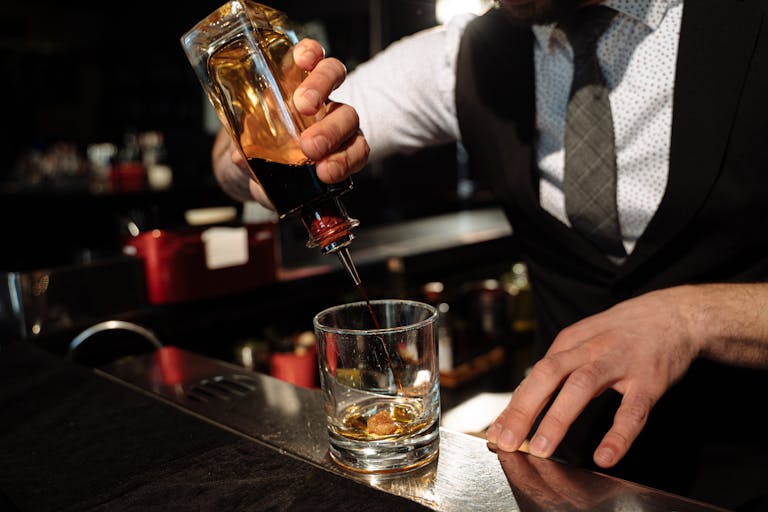 Close-up of bartender pouring whiskey into a glass at a bar counter.