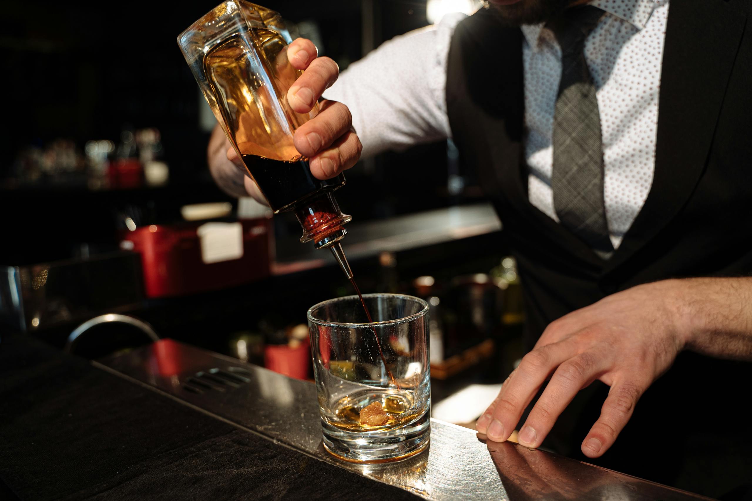 Close-up of bartender pouring whiskey into a glass at a bar counter.