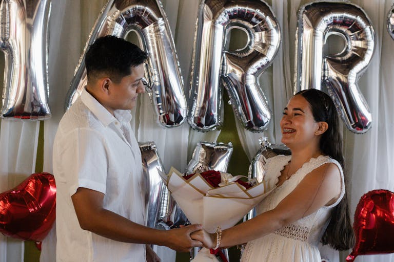 Couple celebrating engagement with balloons and bouquet indoors. Joyful and festive atmosphere captured.