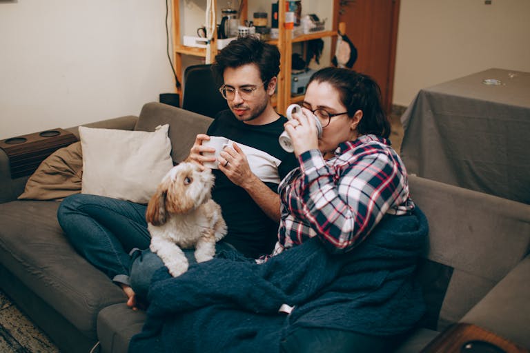 Couple enjoying a relaxed evening with coffee and their dog on a cozy couch indoors.