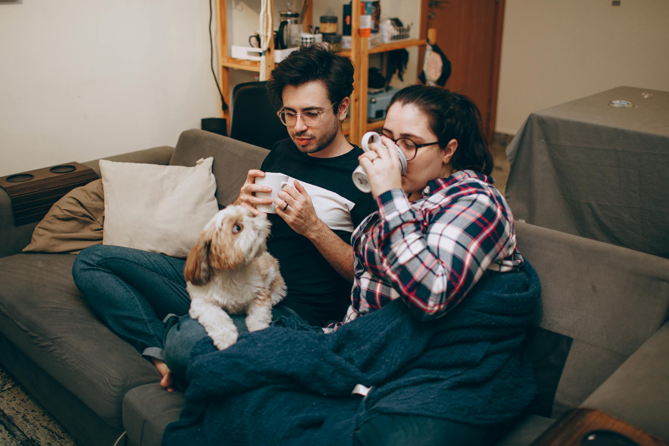 Couple enjoying a relaxed evening with coffee and their dog on a cozy couch indoors.