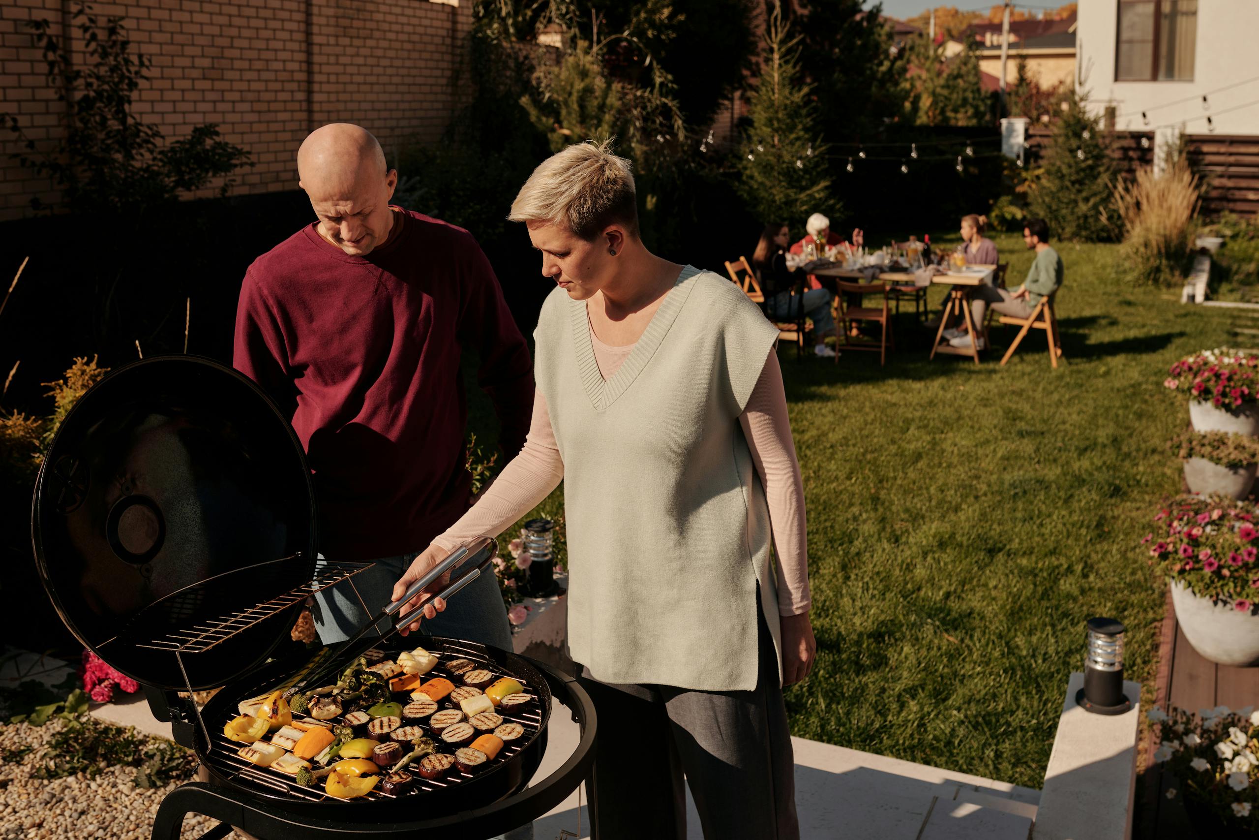 Couple grilling vegetables at a backyard barbecue gathering.