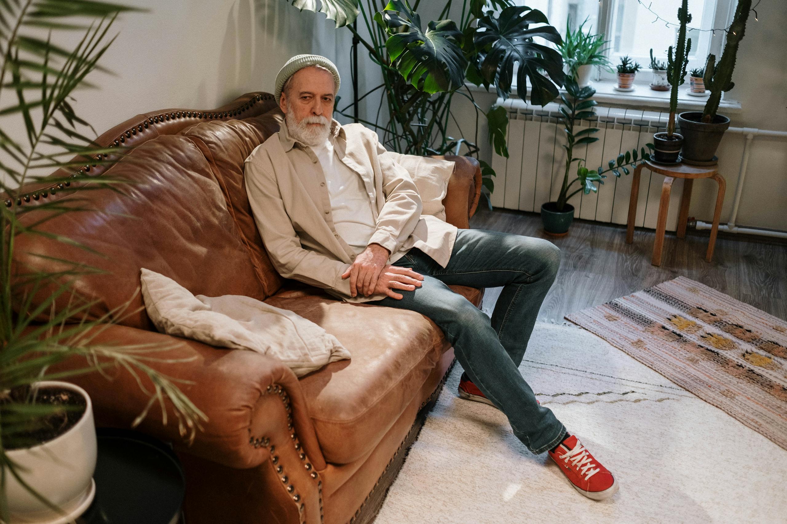 Elderly man relaxing on a leather sofa in a cozy indoor setting with plants.