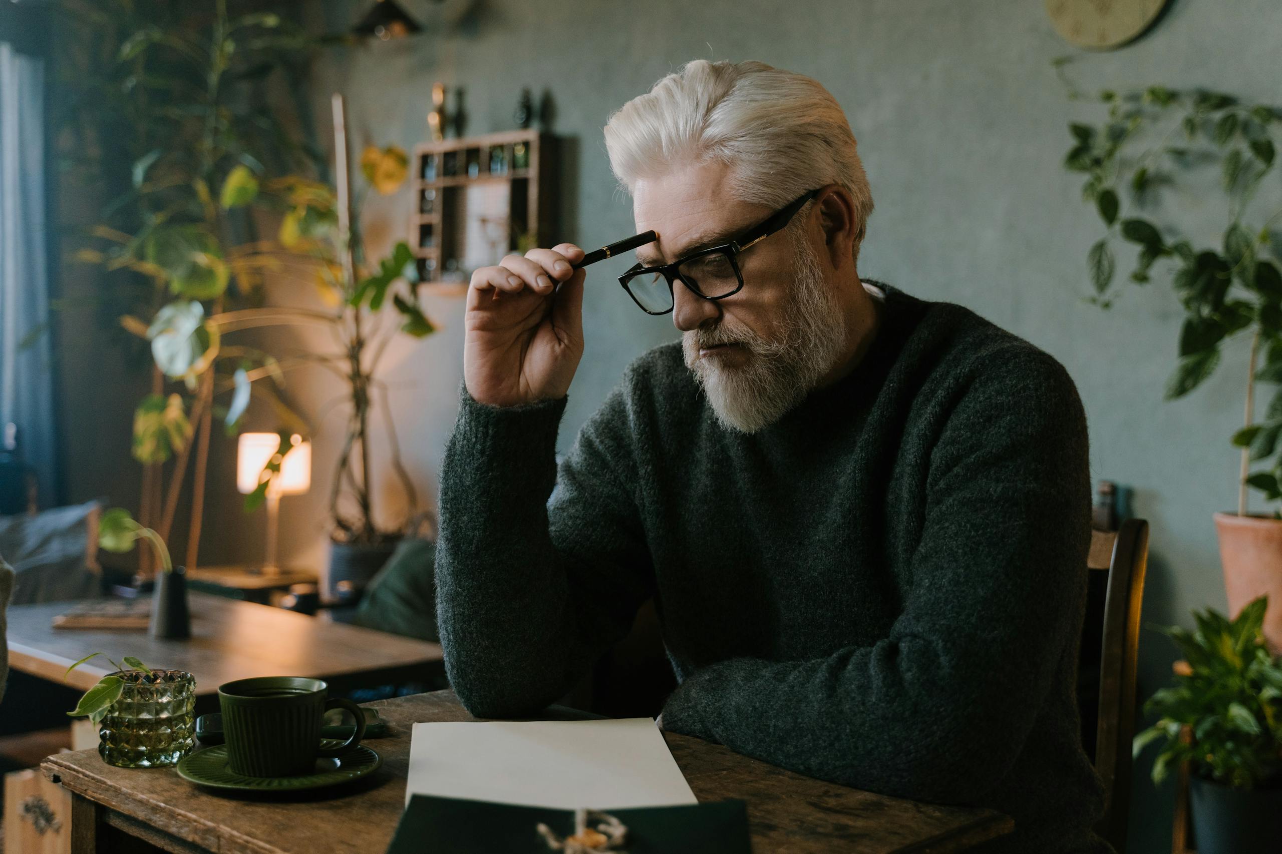 Elderly man with gray hair and beard thinking while sitting at table.