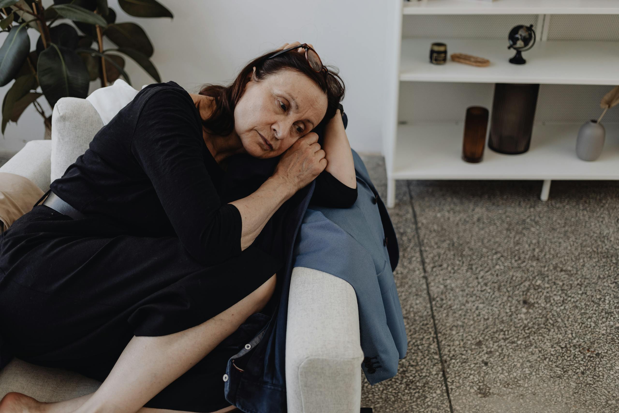 Elderly woman in deep thought, sitting alone on a couch indoors.