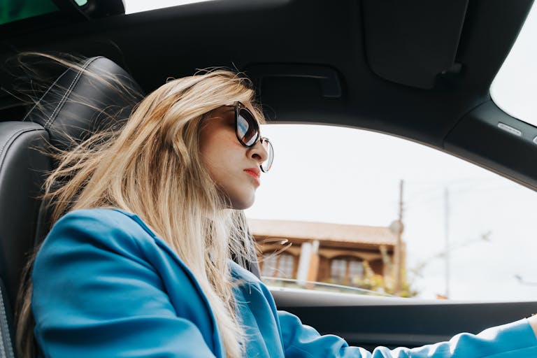 Elegant woman wearing sunglasses is driving through Curitiba, showcasing a modern and stylish look.