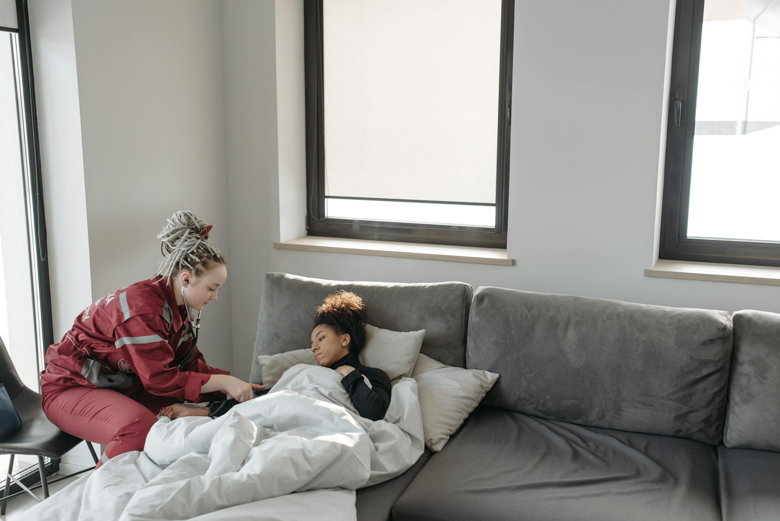 Emergency responder assisting a sick woman on a sofa indoors.