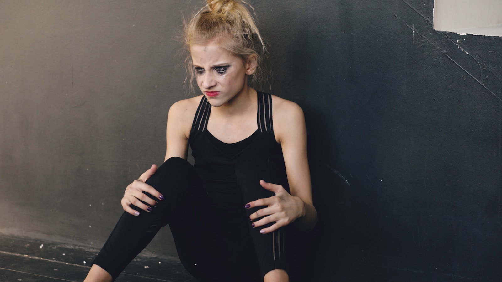 Woman in black sportswear sitting against a gray wall