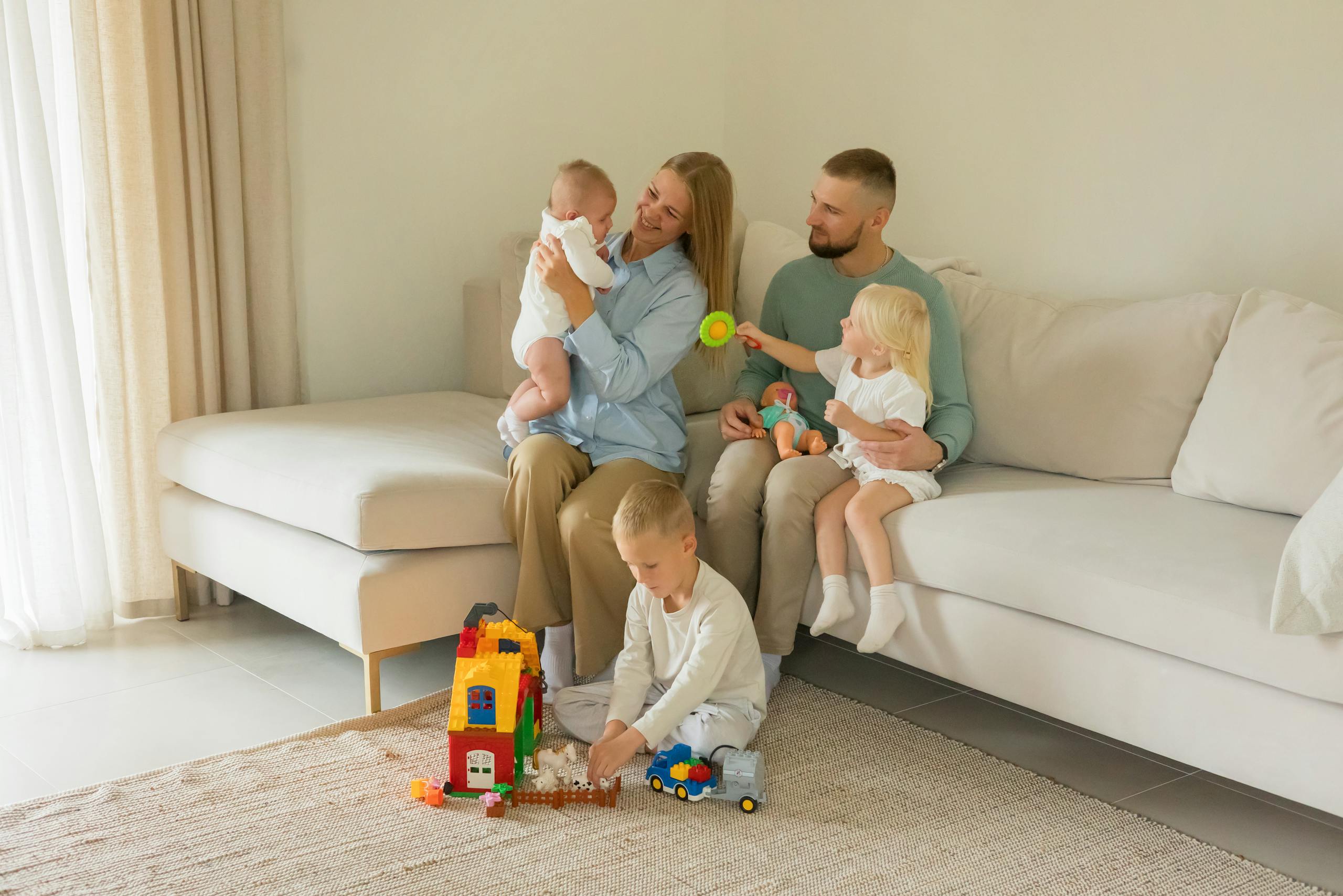 Family enjoying playtime with children and toys on a cozy sofa indoors.