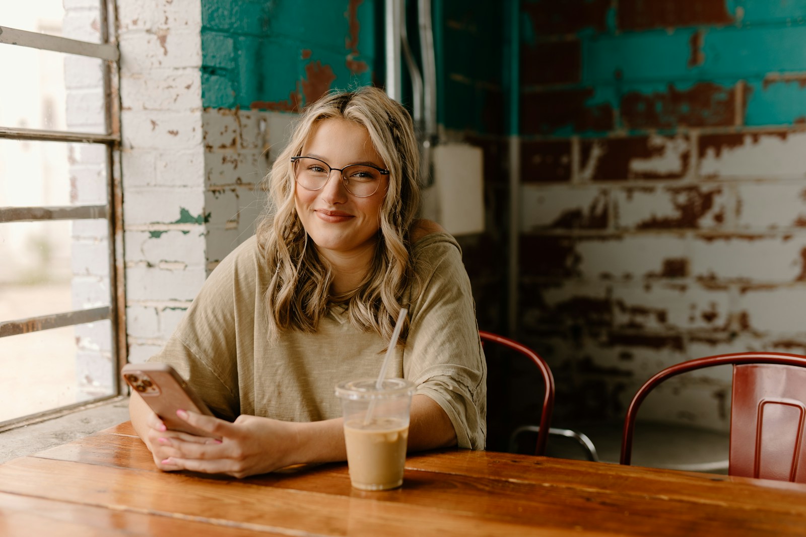 a woman sitting at a table with a drink and cell phone