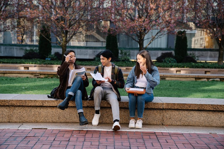 Group of college students laughing and studying outdoors on a campus bench during spring.