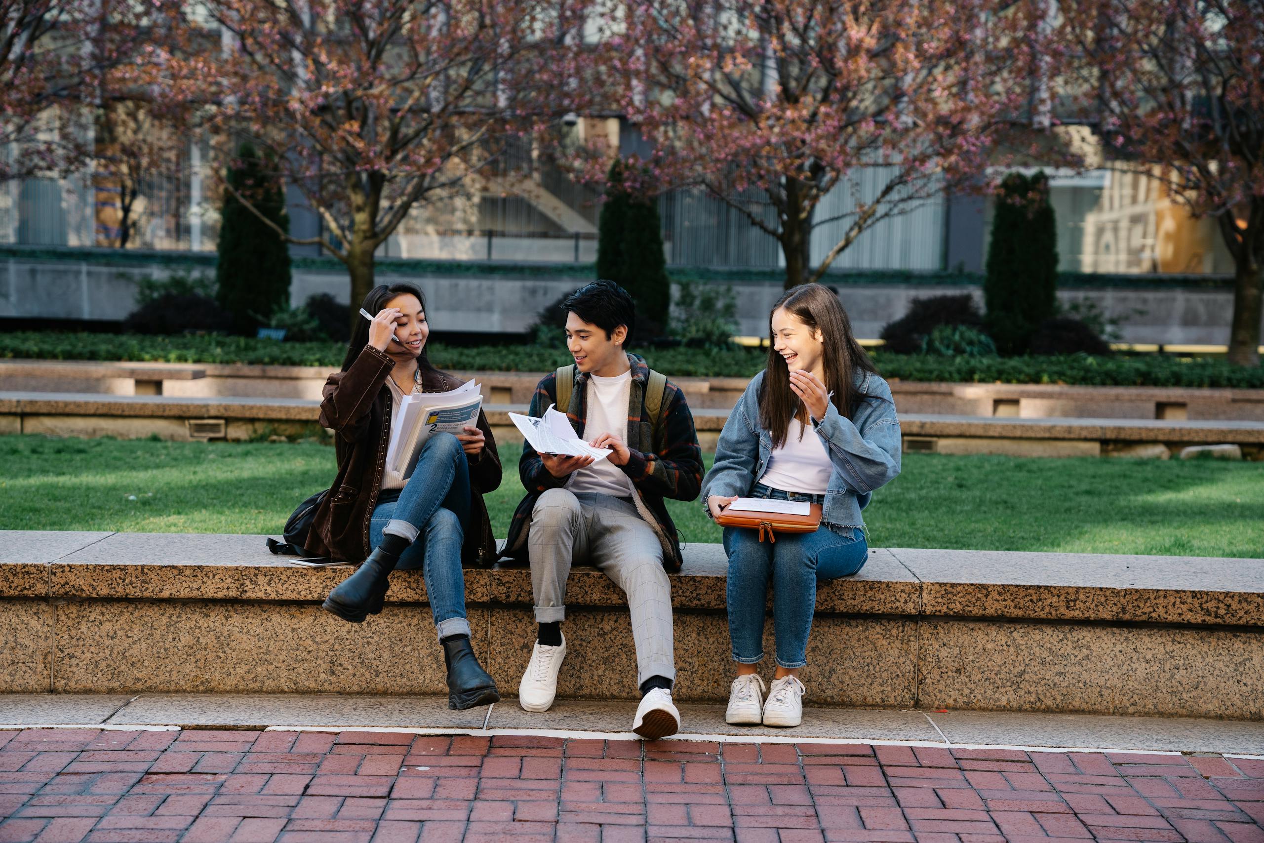 Group of college students laughing and studying outdoors on a campus bench during spring.