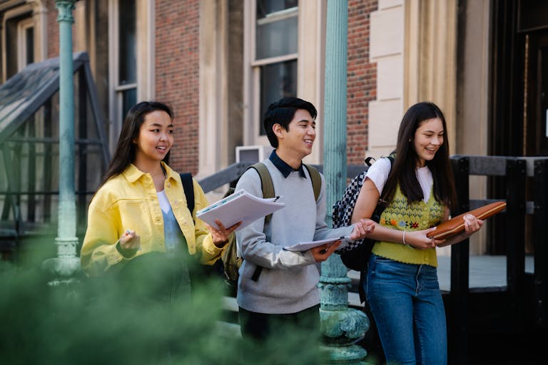 Group of diverse college students walking outdoors and smiling, carrying notebooks and backpacks.