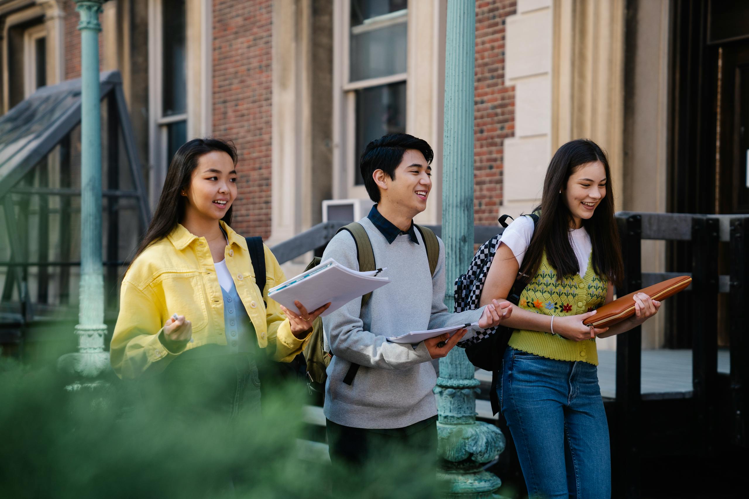 Group of diverse college students walking outdoors and smiling, carrying notebooks and backpacks.