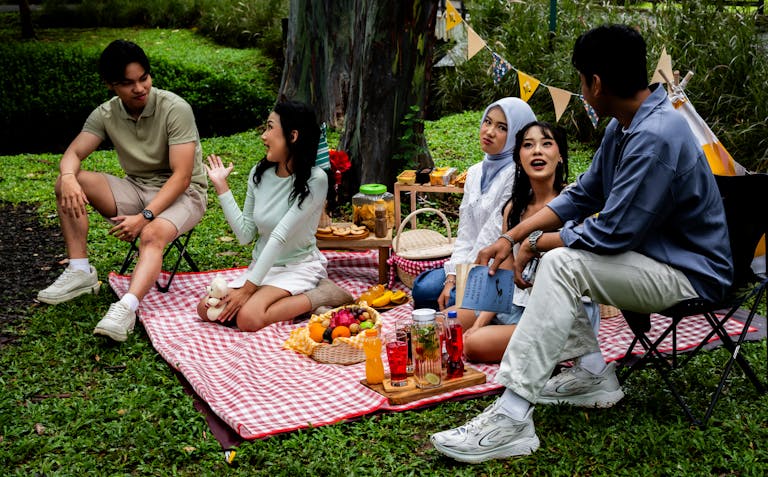 Group of friends enjoying a casual picnic outdoors in a vibrant Indonesian garden setting.
