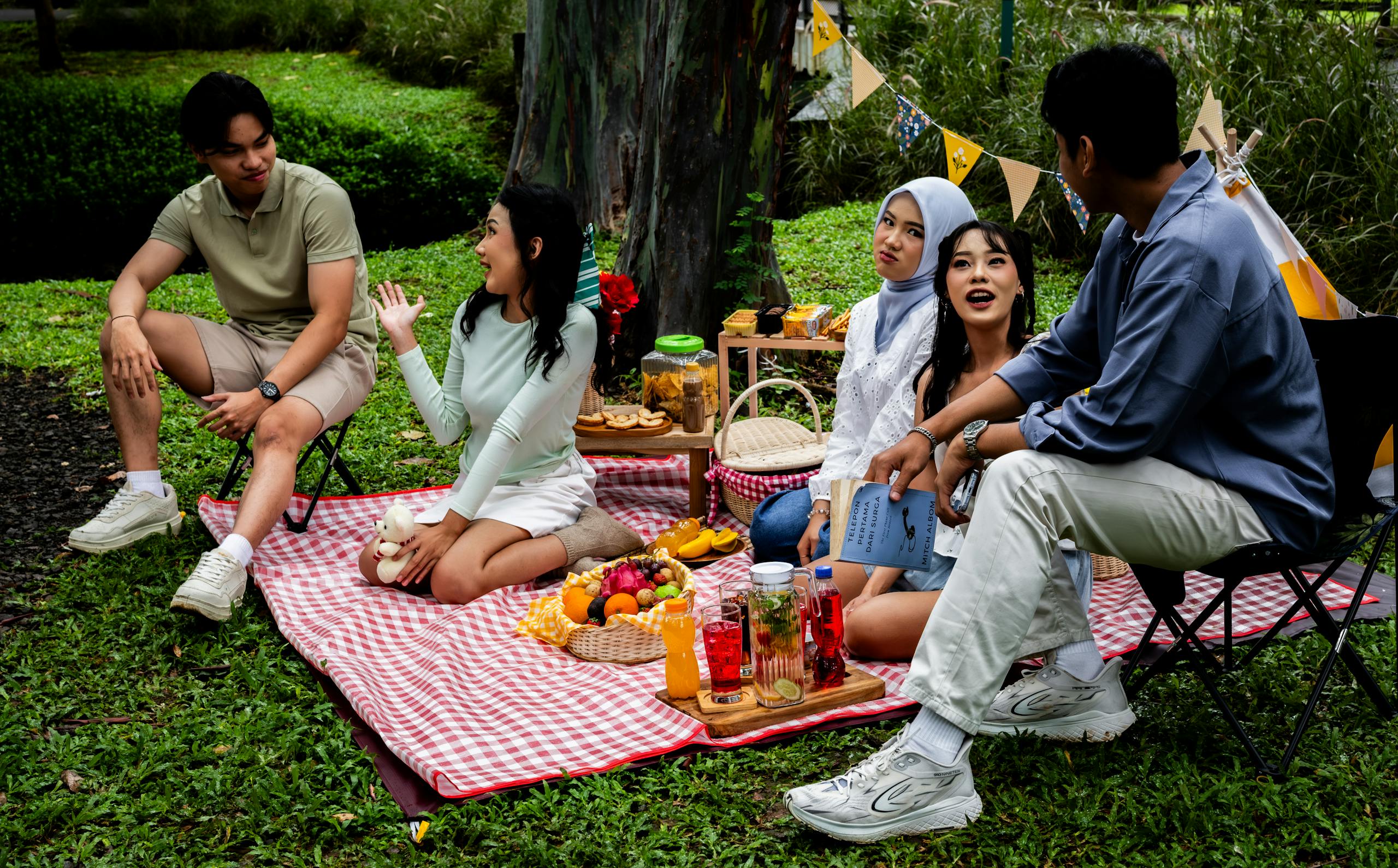 Group of friends enjoying a casual picnic outdoors in a vibrant Indonesian garden setting.